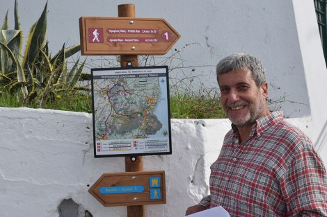 Ο κ. Κώστας Ζαρόκωστας, που εθελοντικά διαμόρφωσε το πρόγραμμα Χαρτογράφησης, Συντήρησης & Σήμανσης των παλιών δρόμων και των μονοπατιών για λογαριασμό του Δήμου Θήρας, πανευτυχής, δίπλα στην πινακίδα και τις σημάνσεις που ήδη βρίσκονται τοποθετημένες στην πλατεία του Πύργου